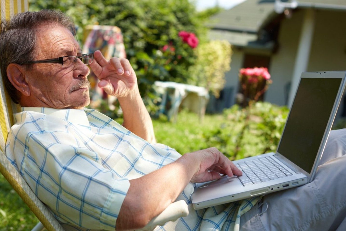 Un señor mayor usa su computadora portátil en el patio de su casa